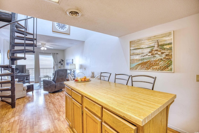 kitchen with a kitchen island, ceiling fan, a breakfast bar, a textured ceiling, and light hardwood / wood-style flooring