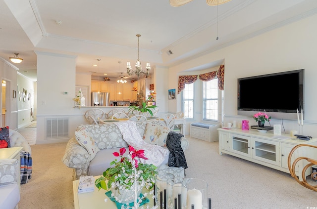 living room with an inviting chandelier, ornamental molding, and a tray ceiling