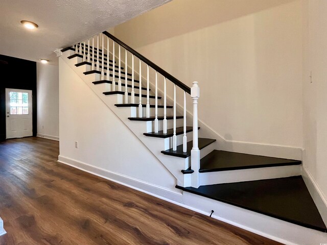 staircase featuring a textured ceiling and dark wood-type flooring