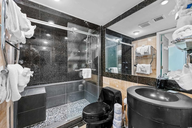 bathroom with a shower with door, toilet, vanity, and tile walls