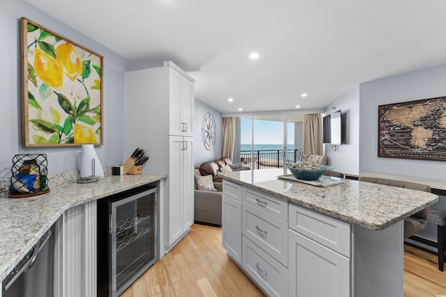 kitchen featuring white cabinetry, a water view, light hardwood / wood-style flooring, beverage cooler, and light stone countertops