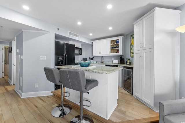 kitchen featuring light wood-type flooring, a kitchen bar, black appliances, and white cabinets