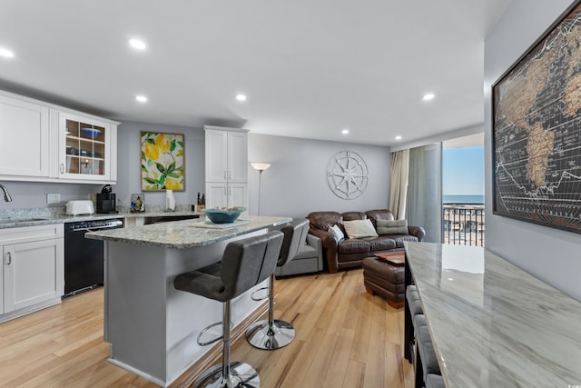 kitchen featuring light hardwood / wood-style floors, a kitchen bar, white cabinetry, dishwasher, and light stone counters