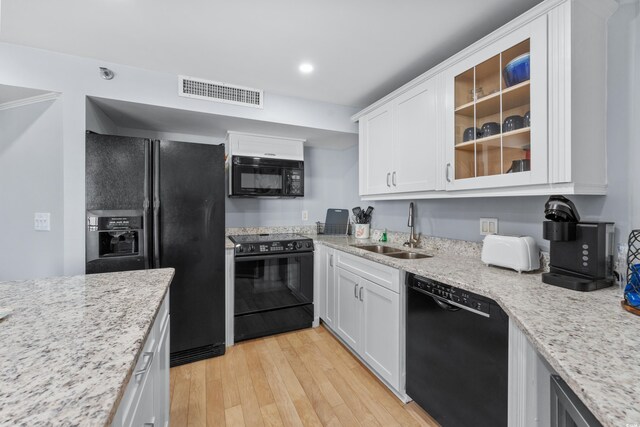 kitchen with sink, white cabinets, light hardwood / wood-style flooring, light stone countertops, and black appliances