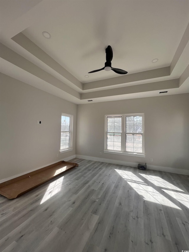 unfurnished room with wood finished floors, visible vents, baseboards, ceiling fan, and a raised ceiling