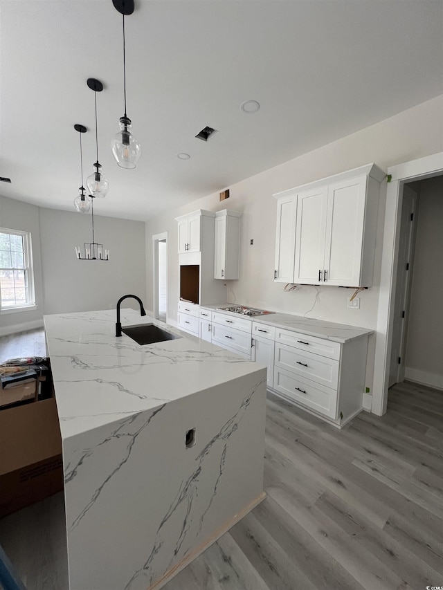 kitchen with light stone counters, light wood finished floors, a sink, cooktop, and white cabinetry