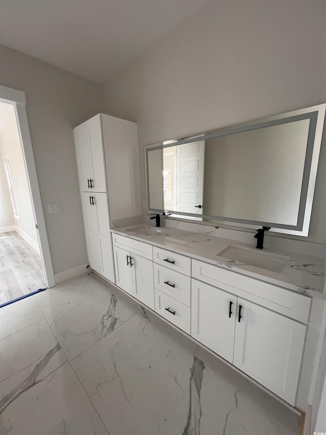 full bath featuring double vanity, marble finish floor, baseboards, and a sink