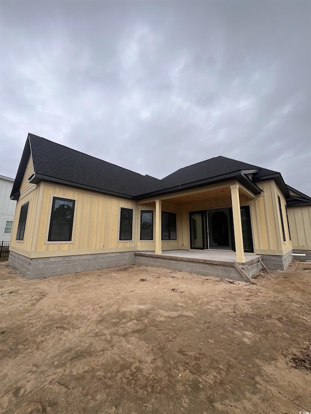 back of property featuring board and batten siding, a shingled roof, and a patio