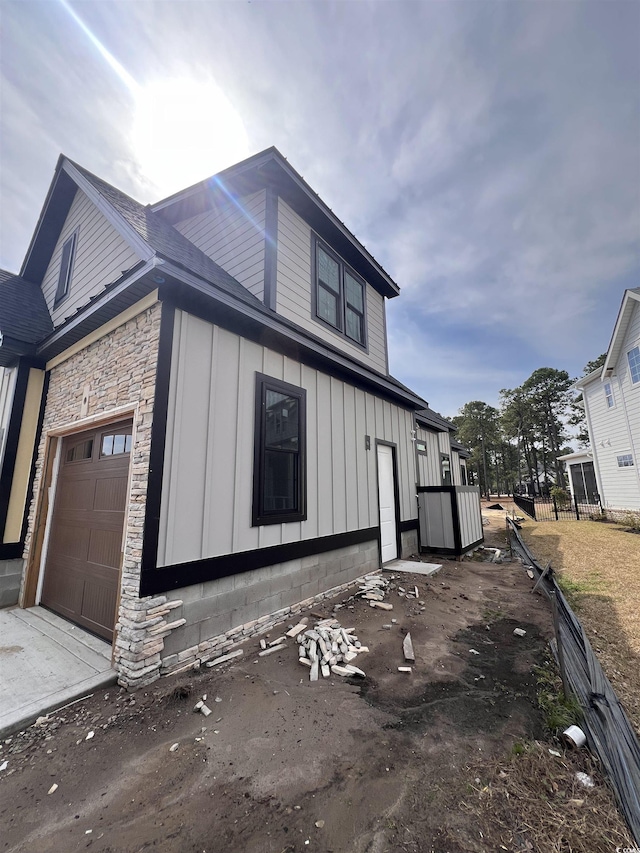 view of home's exterior featuring driveway, stone siding, fence, board and batten siding, and a garage