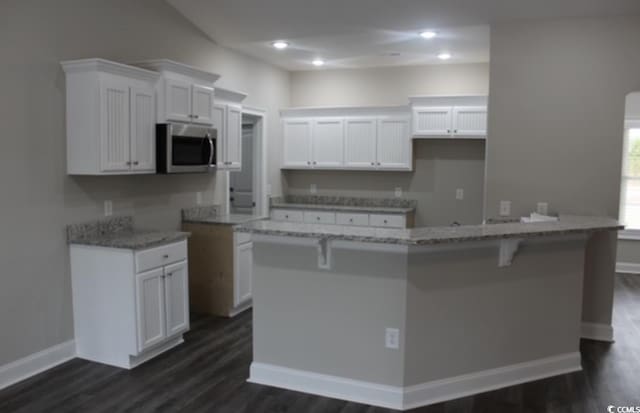 kitchen with stainless steel microwave, white cabinets, dark wood-style flooring, and light stone countertops