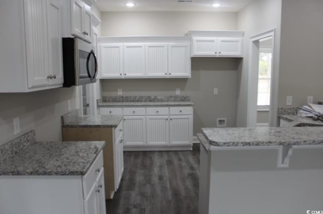 kitchen featuring stainless steel microwave, dark wood-style floors, white cabinetry, a peninsula, and light stone countertops