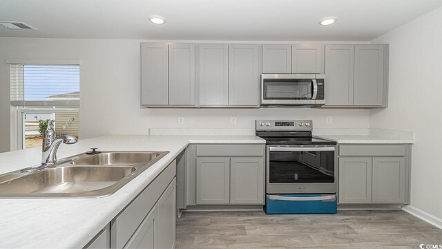 kitchen with gray cabinetry, light hardwood / wood-style floors, sink, and stainless steel appliances