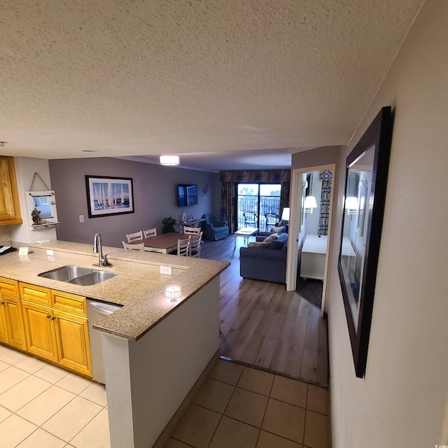 kitchen with sink, stainless steel dishwasher, light hardwood / wood-style flooring, light stone countertops, and a textured ceiling