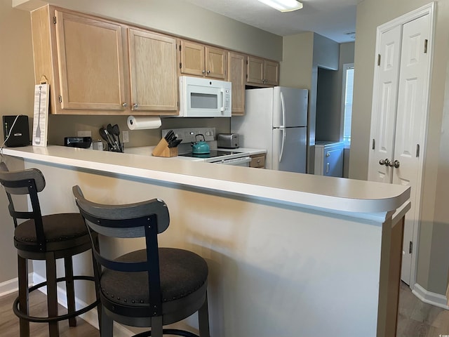 kitchen featuring white appliances, kitchen peninsula, a breakfast bar area, and hardwood / wood-style flooring