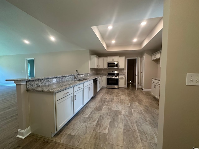 kitchen with white cabinetry, kitchen peninsula, a tray ceiling, appliances with stainless steel finishes, and sink