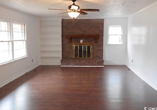 unfurnished living room with a textured ceiling, dark wood-type flooring, built in shelves, and a brick fireplace