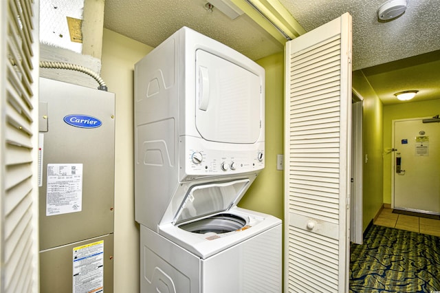 washroom with stacked washer / drying machine, a textured ceiling, and dark tile flooring