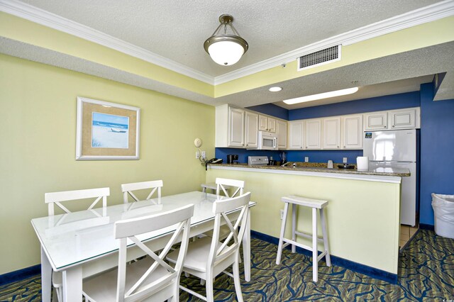 kitchen featuring pendant lighting, a kitchen breakfast bar, a textured ceiling, ornamental molding, and white appliances