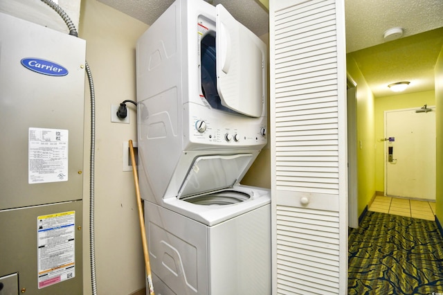 clothes washing area featuring stacked washer and dryer, a textured ceiling, electric dryer hookup, and tile floors