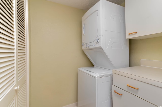 washroom with cabinets, a textured ceiling, and stacked washer and clothes dryer