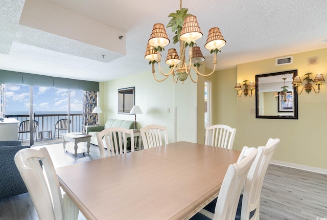 dining room featuring light hardwood / wood-style flooring, a water view, an inviting chandelier, and a textured ceiling