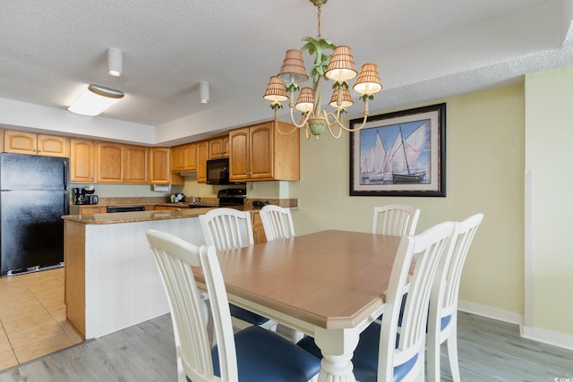 dining room featuring a textured ceiling, a notable chandelier, and light hardwood / wood-style flooring