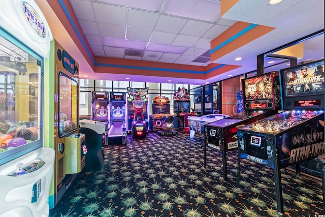 recreation room featuring a drop ceiling, dark colored carpet, and a tray ceiling