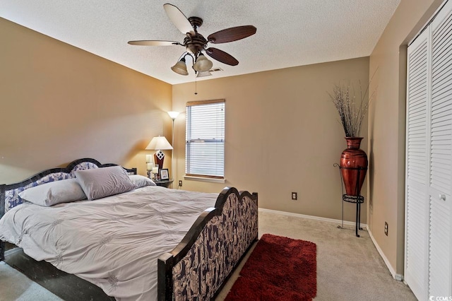 bedroom with a closet, a textured ceiling, ceiling fan, and light colored carpet