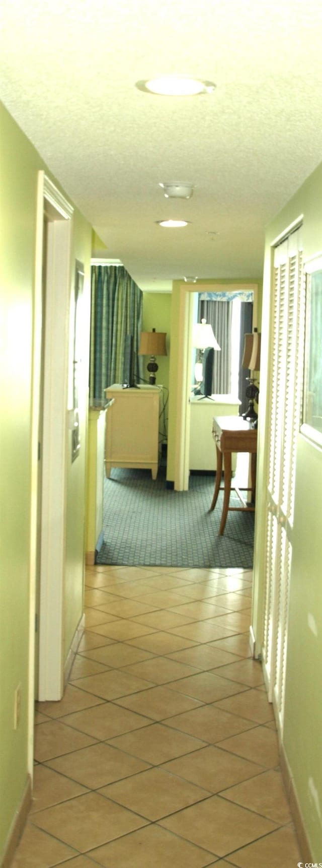 corridor featuring plenty of natural light, a textured ceiling, and light tile floors