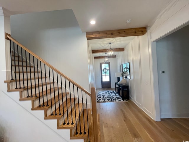 foyer entrance with hardwood / wood-style flooring, beamed ceiling, and a notable chandelier