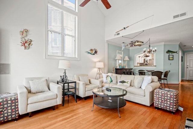 living room with crown molding, a high ceiling, light wood-type flooring, and ceiling fan with notable chandelier