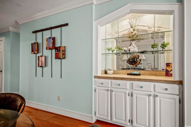 bar with white cabinets, tile counters, ornamental molding, and hardwood / wood-style flooring