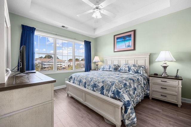 bedroom with ceiling fan, a tray ceiling, and hardwood / wood-style flooring