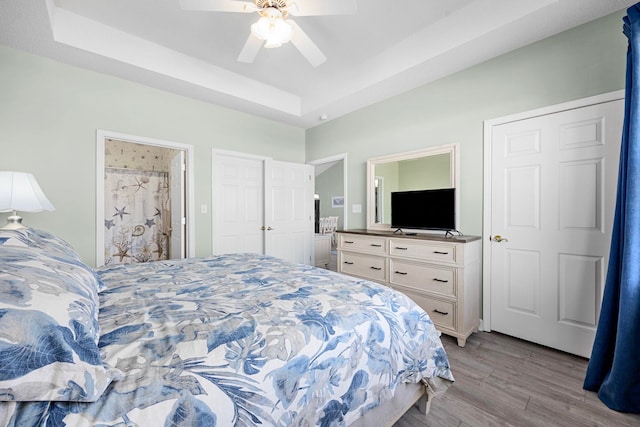 bedroom with a raised ceiling, ceiling fan, hardwood / wood-style floors, and ensuite bathroom