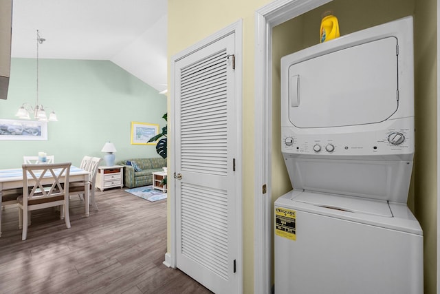 clothes washing area with stacked washer and dryer, a notable chandelier, and hardwood / wood-style flooring