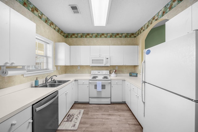 kitchen with sink, white appliances, white cabinetry, and light wood-type flooring