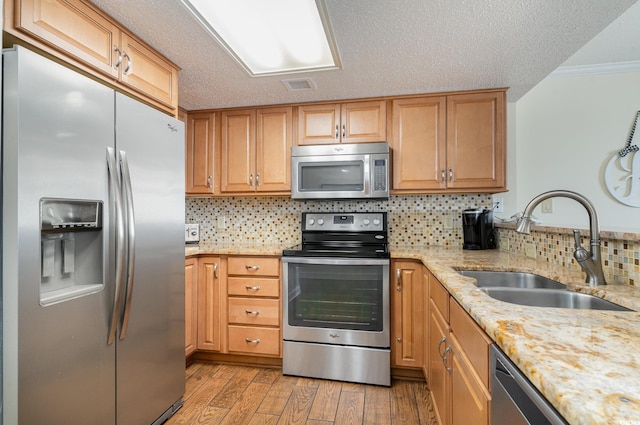 kitchen featuring light stone counters, tasteful backsplash, stainless steel appliances, light wood-type flooring, and sink