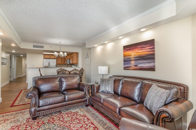 living room with a notable chandelier, a textured ceiling, crown molding, and light hardwood / wood-style flooring