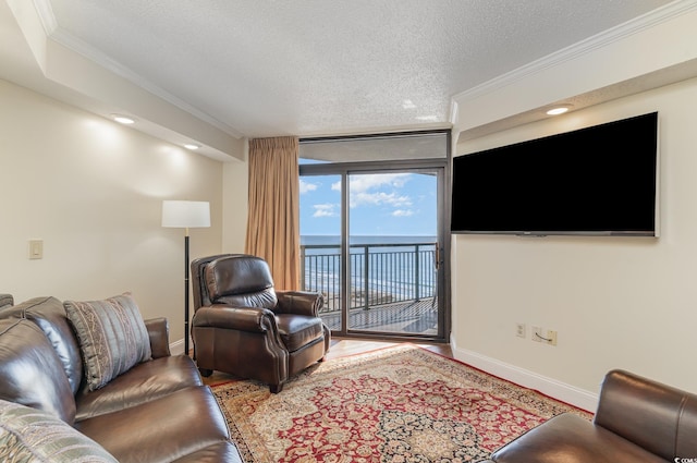 living room featuring a water view, ornamental molding, a textured ceiling, and a wall of windows