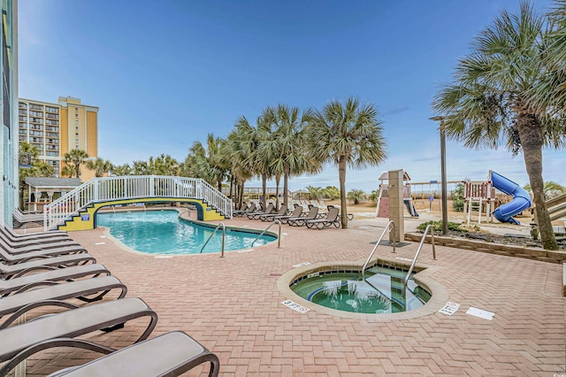 view of swimming pool featuring a playground, a water slide, and a hot tub