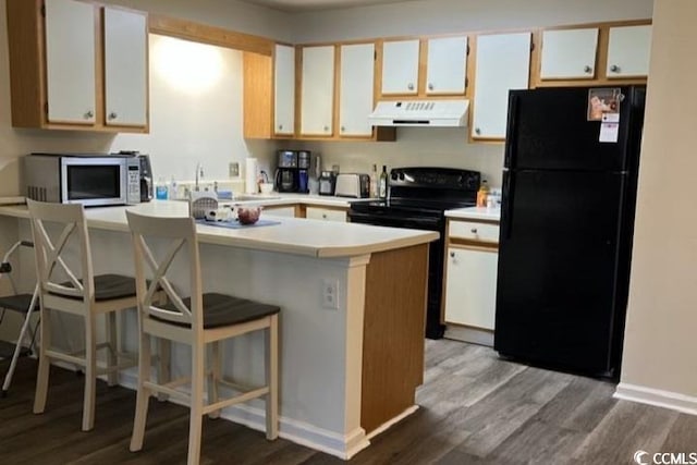 kitchen featuring sink, hardwood / wood-style flooring, a kitchen breakfast bar, black appliances, and white cabinets