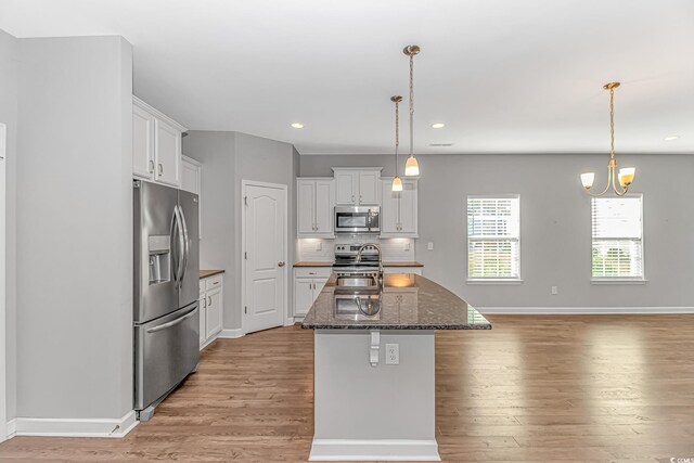 kitchen with a kitchen island with sink, white cabinets, hanging light fixtures, and appliances with stainless steel finishes