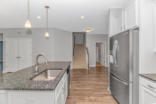 kitchen featuring dark stone counters, stainless steel appliances, a kitchen island with sink, sink, and white cabinets