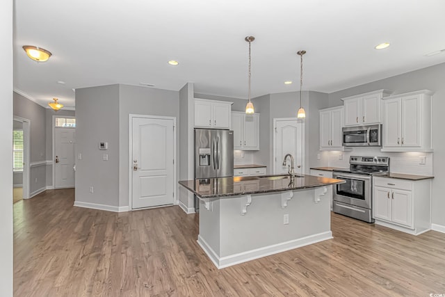 kitchen featuring dark stone counters, a center island with sink, appliances with stainless steel finishes, white cabinetry, and a breakfast bar area