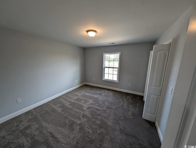 unfurnished room with visible vents, dark carpet, and baseboards