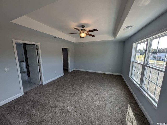 unfurnished bedroom featuring dark colored carpet, visible vents, a raised ceiling, and baseboards