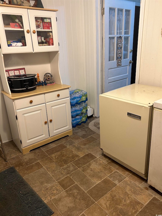 kitchen with white cabinetry, dark tile flooring, and wooden walls