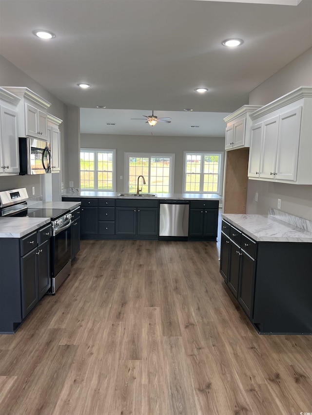 kitchen with a sink, light stone counters, light wood-style floors, appliances with stainless steel finishes, and white cabinets