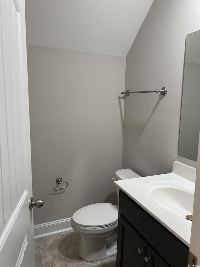 half bathroom featuring vanity, vaulted ceiling, toilet, and baseboards