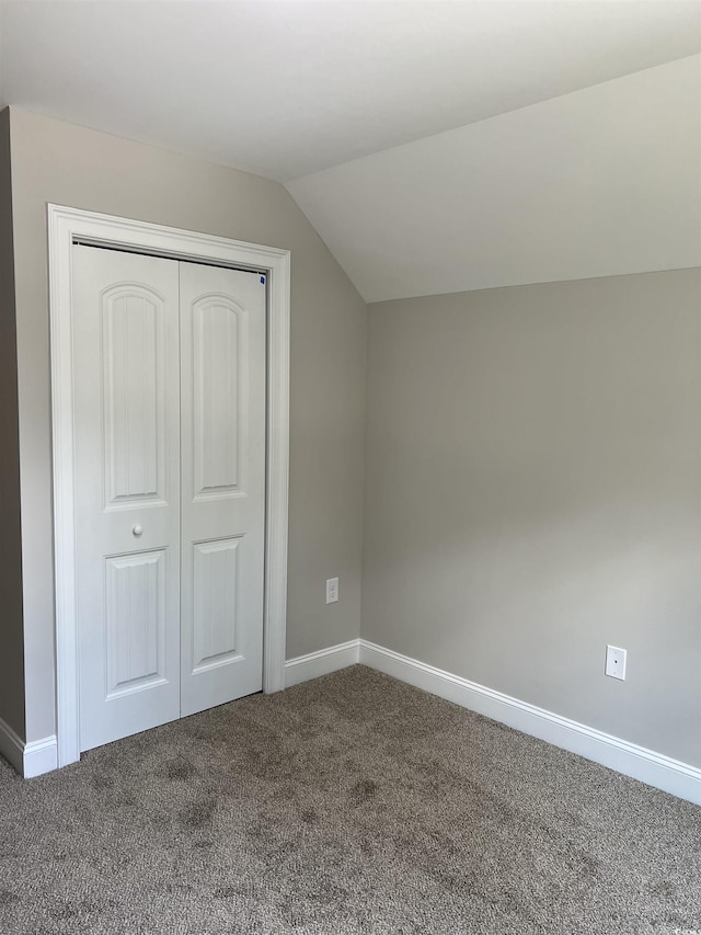 unfurnished bedroom with lofted ceiling, baseboards, a closet, and dark carpet